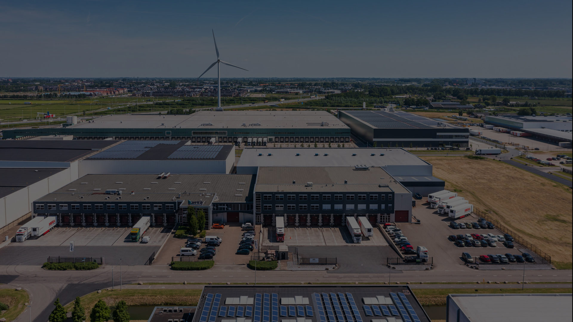 Aerial view of industrial building in Netherlands, meadow and windmill in the background.