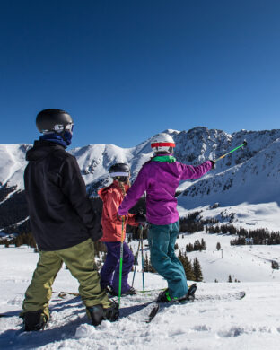 Three children standing at the top of the mountain ready to ski down
